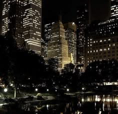 the city is lit up at night with lights reflecting in the water and skyscrapers