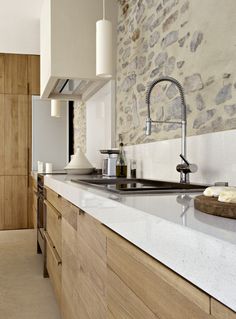 a kitchen with white counter tops and wooden cabinets in front of a stone backsplash