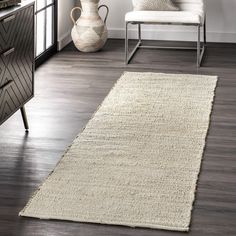 a white rug in a living room next to a chair and table with vases on it