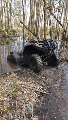 a four - wheeler is stuck in the mud near some trees and water on a muddy path