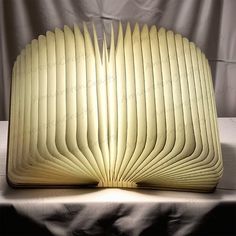 an open book sitting on top of a table next to a white cloth covered wall