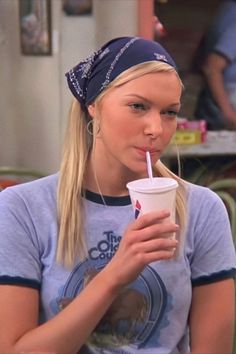 a woman drinking from a cup with a straw in her mouth and wearing a bandana