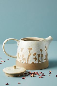 a ceramic tea pot sitting on top of a table next to a cup with lid