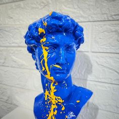 a blue statue with yellow paint splattered on it's face and neck