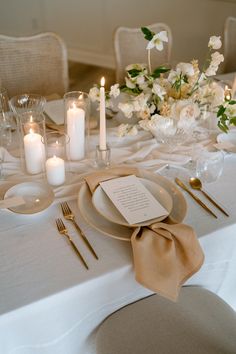 the table is set with white flowers, candles and place settings for an elegant dinner