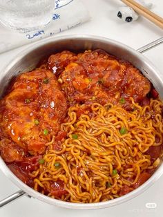 a pan filled with meat and noodles on top of a table next to chopsticks