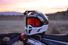 a helmet and goggles sitting on the back of a motorcycle in front of a sunset