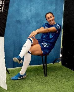 a female soccer player sitting on a chair in front of a blue wall and posing for the camera