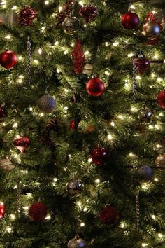 a christmas tree with red and silver ornaments on it's branches is lit up at night