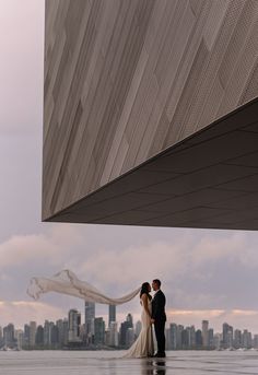 a bride and groom standing in front of a building with the city skyline behind them