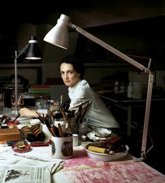 a woman sitting at a desk with lots of art supplies