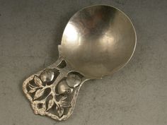 an antique spoon with fruit and leaves carved into the side, on a gray surface