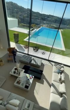 a living room filled with furniture next to a large window overlooking a swimming pool on top of a lush green hillside