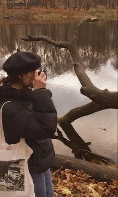 a woman standing next to a lake while talking on a cell phone and holding a bag