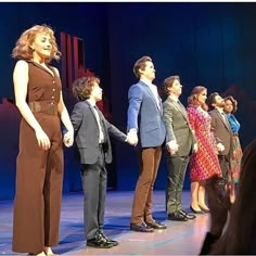 a group of people standing on top of a stage next to each other holding hands