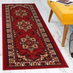 a red area rug with an ornate design on the floor next to a yellow chair