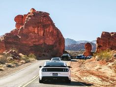 two cars driving down the road in front of large rocks