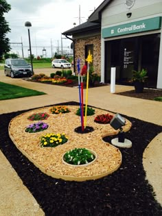 a clock made out of flowers in front of a bank building with cars parked nearby