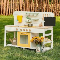 an old fashioned wooden toy kitchen with sunflowers in the grass next to it