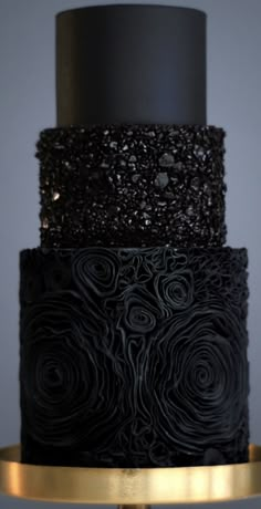 a three tiered black and gold wedding cake with flowers on it's side