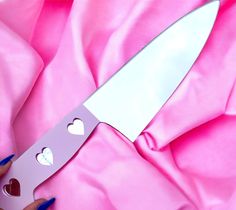 a person holding a knife with hearts cut out of it's blade on pink fabric