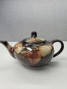 a ceramic teapot with a lid and handle on a white counter top, in front of a gray wall