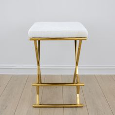 a gold stool with a white cushion sits on a hard wood floor in front of a white wall