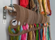 several different colored yarns are hanging on the wall and there is a sewing hook in front of them