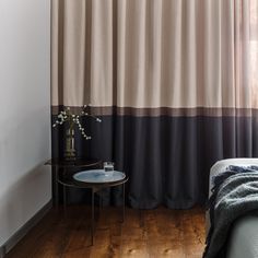 a bed sitting next to a window in a room with wooden floors and curtains on the windowsill