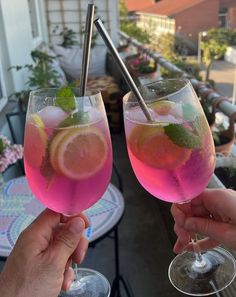 two people holding up wine glasses filled with pink liquid and lemon slices on the outside patio