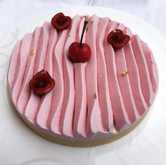 a cake with pink icing and cherries on top is sitting on a white plate