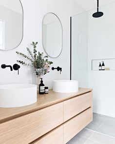 a bathroom with two sinks and mirrors on the wall next to a plant in a vase