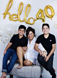 three people sitting on a couch in front of balloons and the word hello spelled out