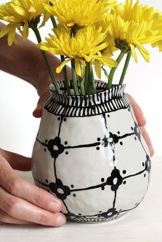 a hand holding a vase with yellow flowers in it