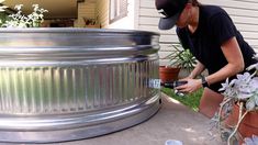 a woman in black shirt and hat working on an outdoor metal planter with potted plants