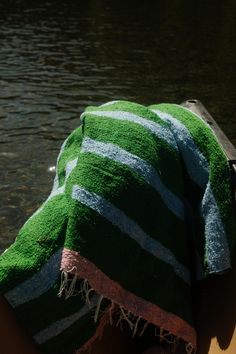 a person wrapped in a green and white striped towel sitting on a bench next to the water