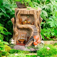 a miniature tree stump house in the middle of some plants and trees with stairs leading up to it