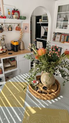 a vase with flowers sitting on top of a table next to a shelf filled with books and knick knacks