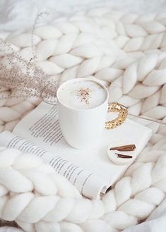 a cup of coffee sitting on top of a white blanket next to a book and some cinnamon sticks