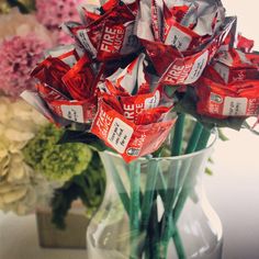 a vase filled with lots of red and silver wrapped candy bar wrappers next to flowers