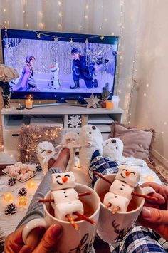 two people are holding mugs with marshmallow faces on them in front of a television