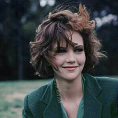 a woman with short hair wearing a suit and smiling at the camera in a park