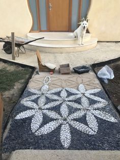 a dog is sitting on the front porch looking at something in the yard that looks like it's made out of stones