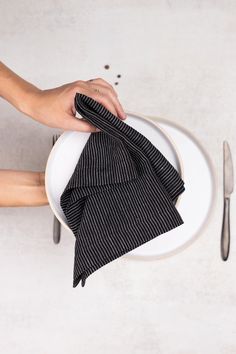 a person holding a napkin on top of a white plate next to a knife and fork