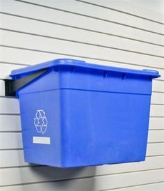 a blue trash can hanging on the side of a building next to a white wall