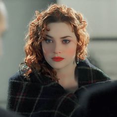 a woman with red hair and blue eyes wearing a black coat looking at another person