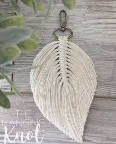 a white tasseled bag hanging from a hook on a wooden surface with leaves