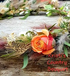 an orange rose sitting on top of a wooden table next to dry grass and feathers