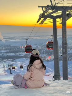 a woman sitting on the snow in front of a ski lift at sunset or dawn