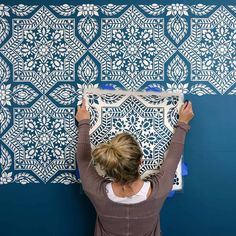 a woman is painting a wall with blue and white stencil designs on it